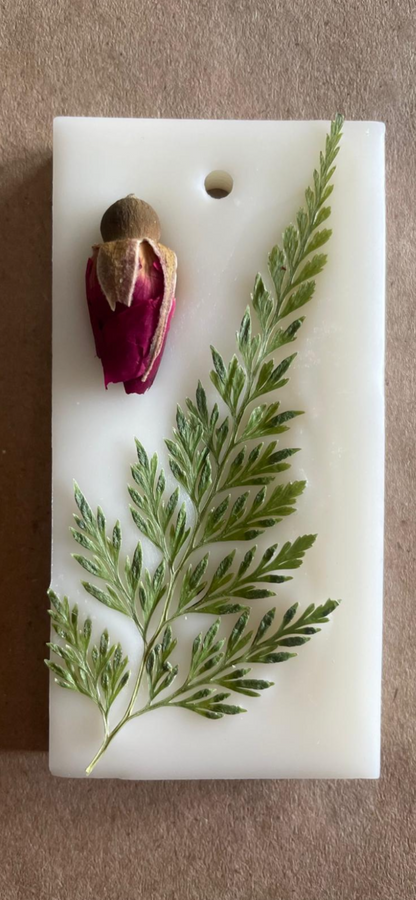 A white rectangular base supports a small figurine of a person holding a flower and pressed fern leaf.
